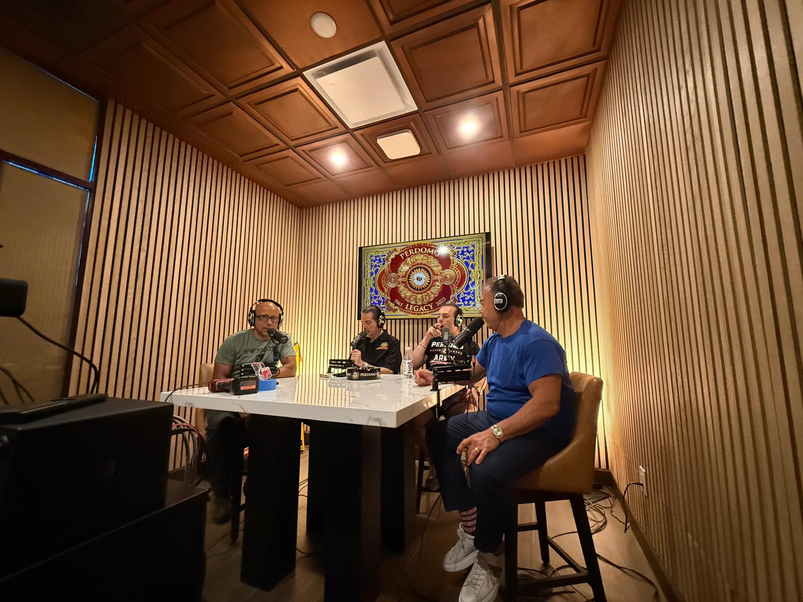 Four people around a marble table with mics and cigars, PERDOMO 1992 LEGACY 2022 wall art behind them